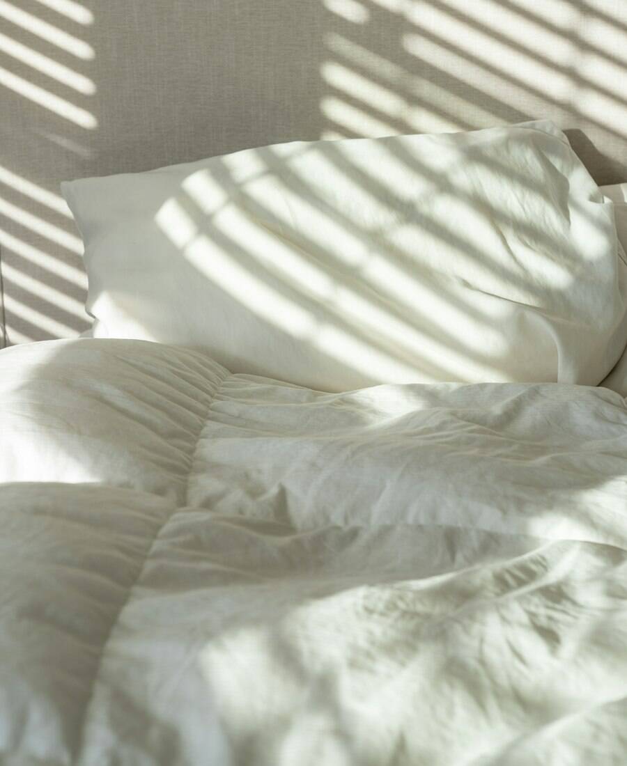 A freshly made bed with crisp white linens in morning sunlight.