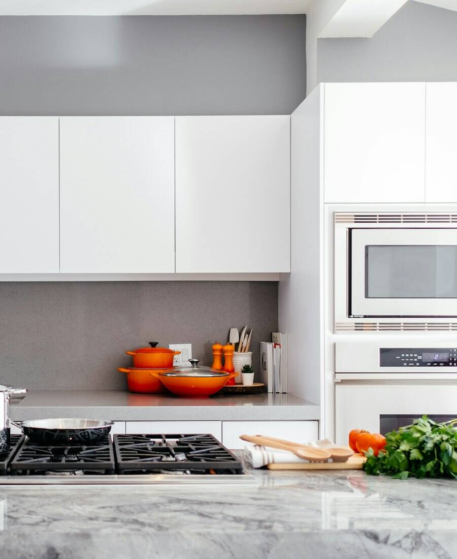 A clean white kitchen with a marble counter and a gas cooktop.